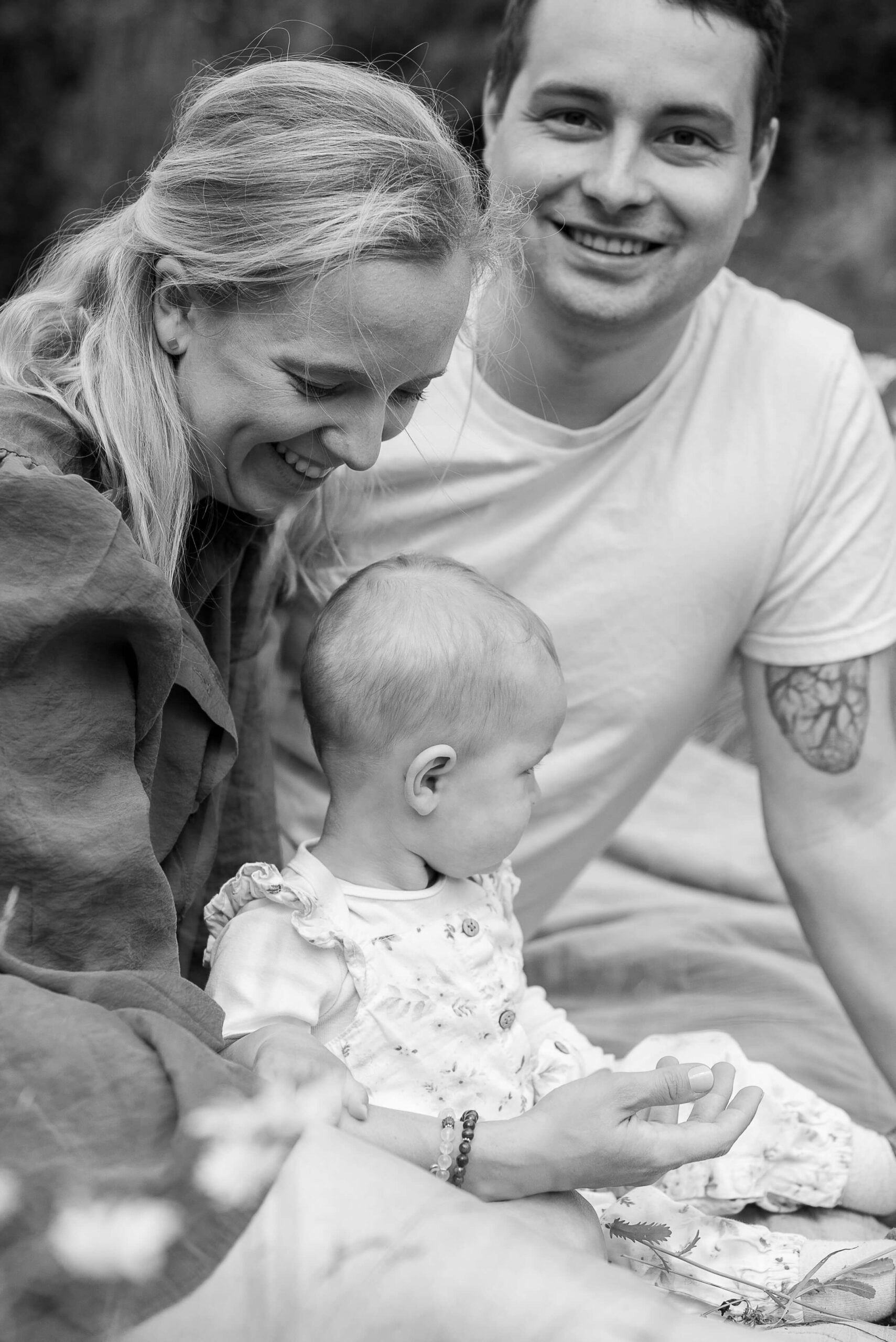 Newbornfotos Zuhause Eine Familie sitzt zusammen im Garten auf einer Decke